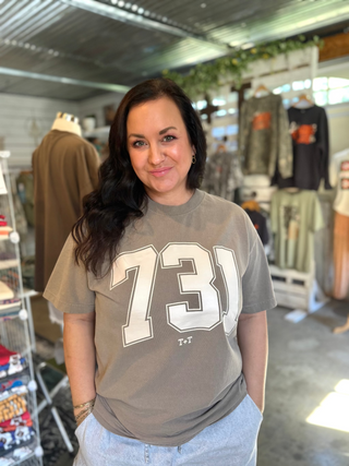 founder Crystal Tucker of Tucked & Threaded wearing a brown graphic tee reading 731 in a cream ink inside her she-shed