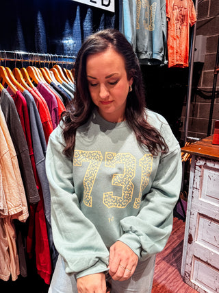 Woman wearing a cypress green color sweatshirt with '731' design printed on it in a clothing store.