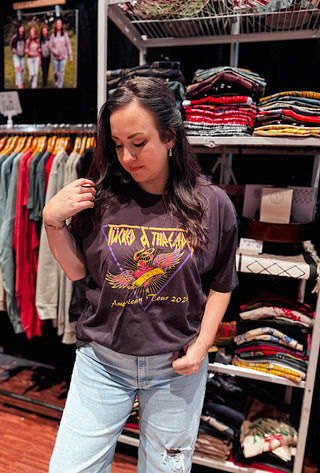 Woman wearing a graphic t-shirt in a store setting with clothing racks in the background