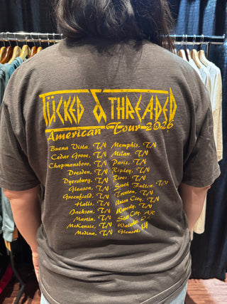 Person wearing a gray t-shirt with yellow text and logos, sitting on a chair.