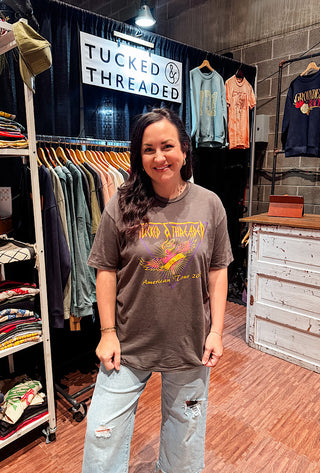 Woman wearing a 'Tucked & Threaded' t-shirt in a clothing store.