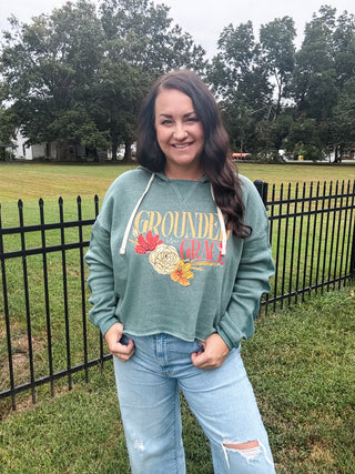 Woman wearing a green sweatshirt with text and graphics, standing outdoors near a fence and trees.