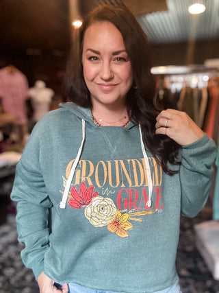 teal hoodie with floral design and text reading "grounded in grace". hoodie has a boxy fit with a feminine look