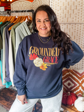 Woman wearing a navy sweatshirt with 'Grounded in Grace' text and floral design in a clothing store.