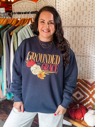 Woman wearing a navy sweatshirt with 'Grounded in Grace' text and floral design in a clothing store.