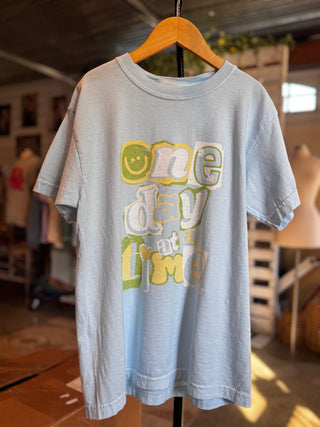 Sky blue youth graphic tee that reads “one day at a time” with a retro vibe for children
