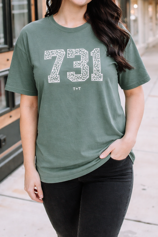 Woman wearing a green t-shirt with '731' printed on it, standing on a sidewalk.