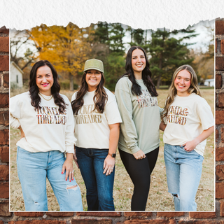 Four women wearing matching sweatshirts with text, standing outdoors in a field.