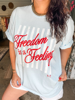Person wearing a light blue t-shirt with 'Freedom is a Feeling' text in red.