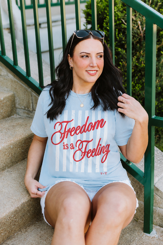 Woman sitting on steps wearing a t-shirt with 'Freedom is a Feeling' text.