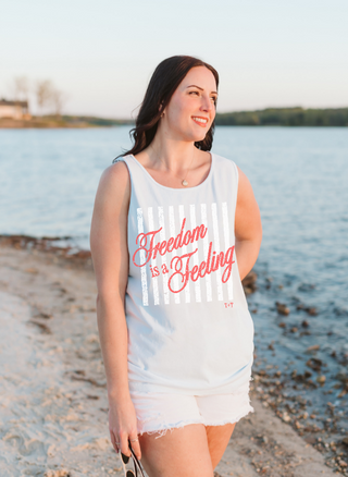 Woman on a beach wearing a tank top with 'Freedom is a Feeling' text