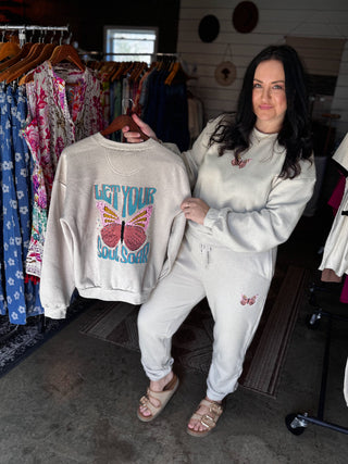 Woman holding a sweatshirt with a butterfly design in a clothing store.