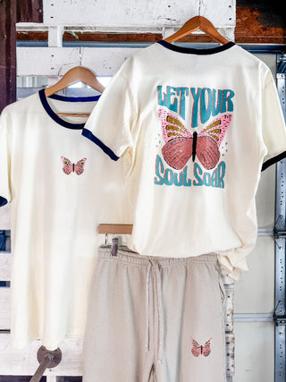 White t-shirt with butterfly design and text 'Let Your Soul Soar' on a hanger.
