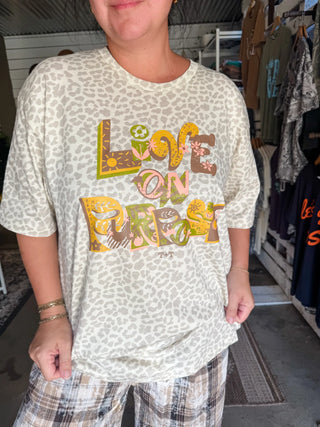 female model in a she-shed wearing work out shorts with a graphic tee in a solid leopard natural color with a graphic design printed on the front in plum, gold, coral, and green inks that reads "live on purpose". shirt is paired with brown and tan plaid pants