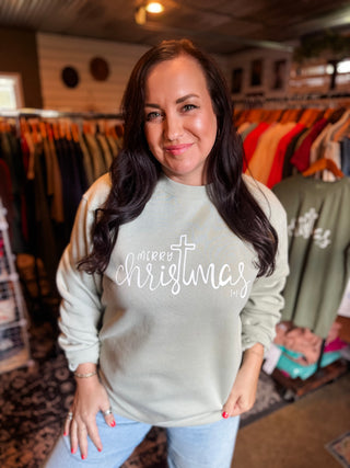 Woman wearing a 'Merry Christmas' sweater in a clothing store. Faith-based design.