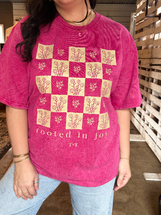 Person wearing a pink t-shirt with floral patterns and text, standing in an indoor setting.