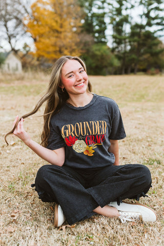 Person sitting in a field wearing a 'Grounded' t-shirt with autumn-themed design.