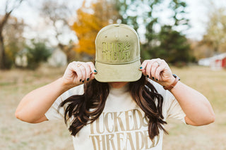 female model wearing an olive green corduroy trucker hat with embroidery in a darker green threaded with the "tucked & threaded" logo