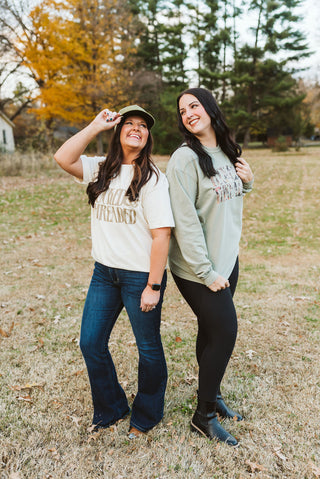 two female models modeling graphic tees with a solid khaki and one with a camouflage print that reads "tucked & threaded"