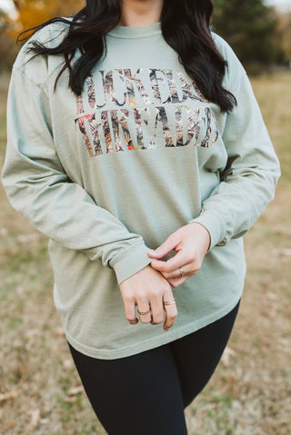 Person wearing a light green long-sleeve shirt with a graphic design in an outdoor setting