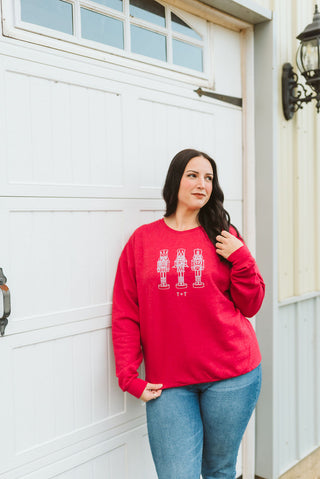 Woman wearing a red sweatshirt with a design standing in front of a white garage door.