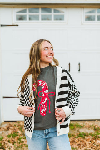 Woman wearing a checkered cardigan over a graphic t-shirt in front of a white building.