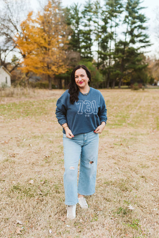 female model wearing a denim blue sweatshirt with white threaded embroidered on the sweatshirt. the design is a 731 area code design.