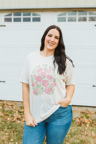 Woman wearing a white t-shirt with pink floral design and text, standing in front of a white garage door.