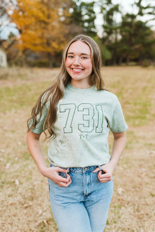 female model wearing a comfort colors colorblast green short-sleeve t-shirt with a 731 design embroidered in a darker green thread