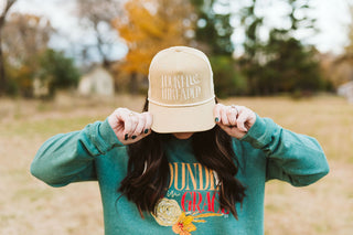 female model wearing a tan corduroy trucker hat with an embroidery design that reads "tucked & threaded" in a lighter tan thread