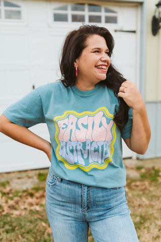 steel blue denim color short-sleeve graphic t-shirt with a printed design in yellow, pink, and purple ink that reads "easily distracted"