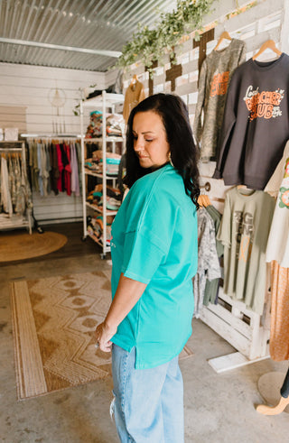 female model showing side view of the teal graphic tee that is longer in the back than the front with side slits